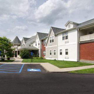 A residential building with a parking lot, featuring accessible parking spaces and a cloudy sky overhead.