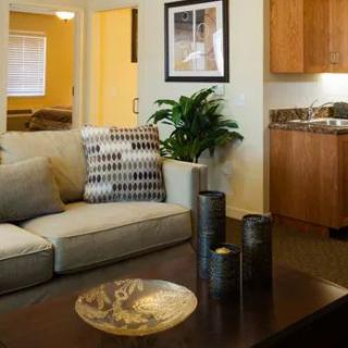 A cozy living room featuring a plush sofa, decorative cushions, and a coffee table, with a kitchenette in the background.