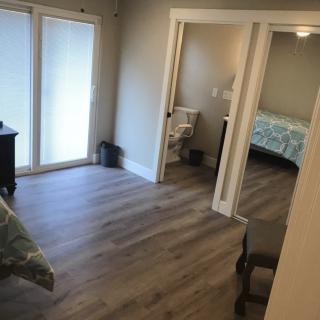 A modern bedroom with wood flooring, featuring a bed, furniture, and an en-suite bathroom.