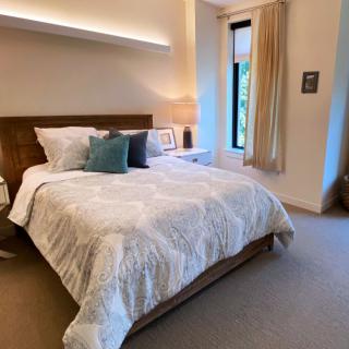 A cozy bedroom featuring a neatly made bed with decorative pillows, a bedside lamp, and a window with curtains.