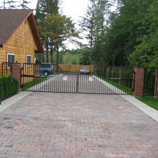 A gated driveway leading to a house surrounded by trees.