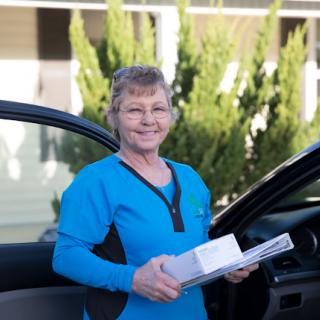 A smiling delivery person standing by a car, ready to deliver packages.