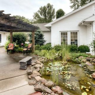 A serene backyard featuring a pond, lush landscaping, and a pergola with cozy seating.