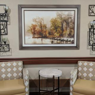 A cozy seating area featuring soft chairs, a small table, and a nature-themed painting.