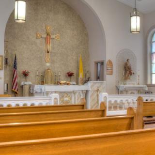 Interior of a church showcasing wooden pews and the altar with a crucifix.