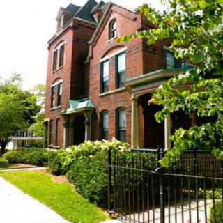 A red brick residential building with greenery and a black metal fence.