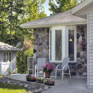 A cozy porch with two chairs and vibrant flowers, set against a stone wall.