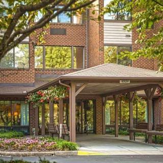 A building entrance with a wooden canopy surrounded by trees and flowers.