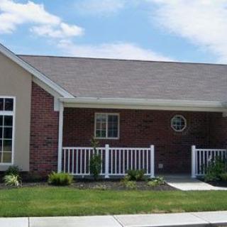 A suburban brick house with a small front yard and white fencing.