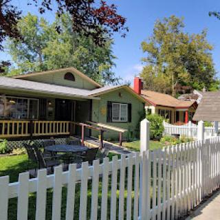 A charming neighborhood scene featuring two houses with a white picket fence and lush greenery.