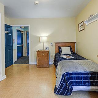 A cozy bedroom with a single bed, nightstand, and lamp, featuring a simple and inviting decor.