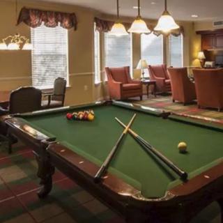 A cozy game room featuring a pool table with cues and balls set up, surrounded by comfortable seating and soft lighting.