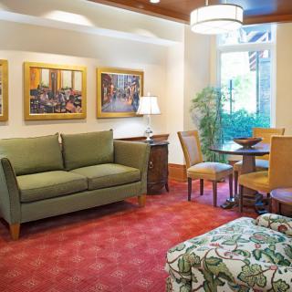 A cozy living room featuring a green sofa, chairs around a small table, decorative artwork on the walls, and an indoor plant under warm lighting.