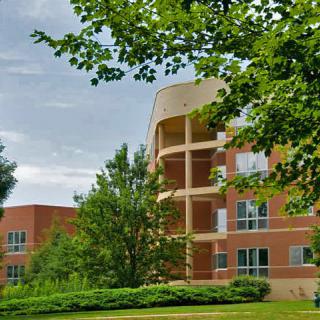A modern brick building surrounded by lush green trees and shrubs under a cloudy sky.