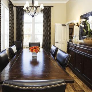 A beautifully set dining room with a large wooden table and upholstered chairs, featuring a chandelier and elegant curtains.