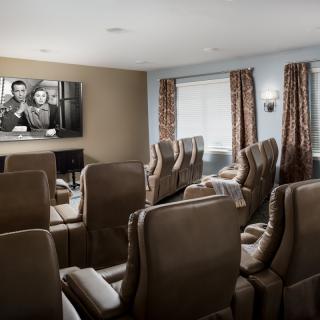 A cozy home theater room with multiple reclining seats facing a large screen showing a black-and-white movie.