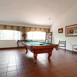 A well-lit billiard room featuring a classic pool table on tiled flooring with large windows and chairs.