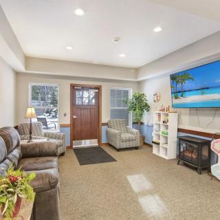 A cozy living room with sofas, a television, and a fireplace, decorated with plants.