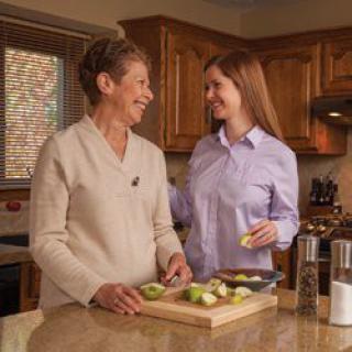 Two women smiling and talking while preparing food in the kitchen.