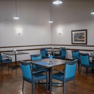 An empty dining area with blue chairs and tables, illuminated by ceiling lights.