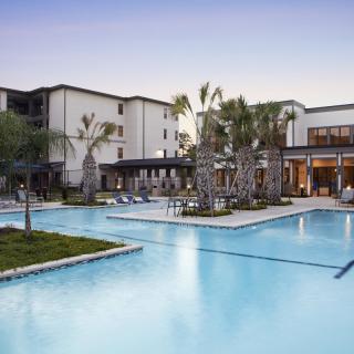 A luxurious hotel resort featuring a large outdoor swimming pool surrounded by palm trees.