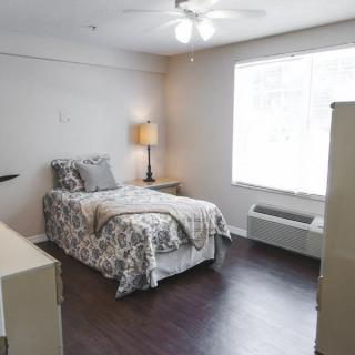 A cozy bedroom with a single bed and minimalist decor, featuring a lamp by the window.