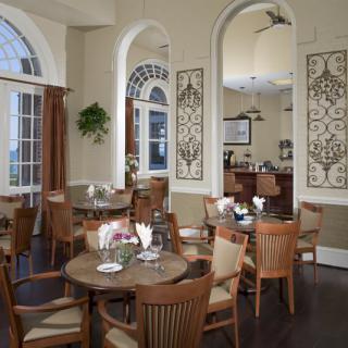 A cozy restaurant interior featuring round tables, wooden chairs, and decorative wall panels with a bar area in the background.