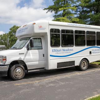 A white shuttle bus parked on the side of a road surrounded by greenery.