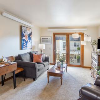 A cozy living room featuring a sofa, coffee table, and artwork on the wall with abundant natural light from large windows.