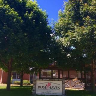 A sign in front of a building surrounded by trees on a sunny day.
