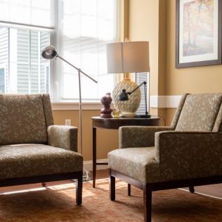 A cozy living room setup featuring two armchairs, a side table with a lamp, and a window allowing natural light to brighten the space.