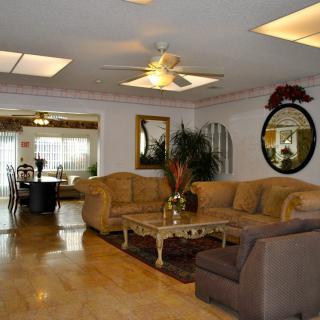 A spacious and elegantly furnished living room featuring a large sofa, a coffee table, and decorative elements such as mirrors and plants.