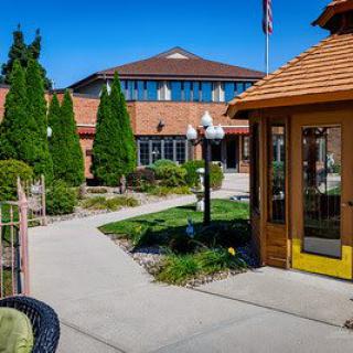 A scenic pathway leads through a landscaped garden towards a brick building under a clear blue sky.