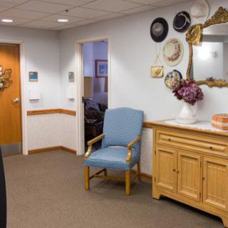 A cozy waiting room area featuring a blue chair, decorative wall plates, and a wooden cabinet with a mirror above it.