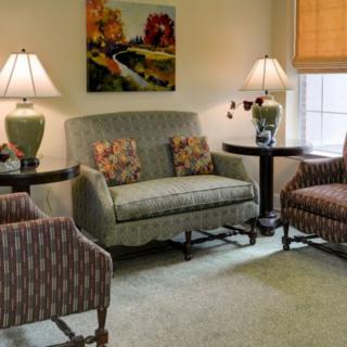 A cozy living room with a sofa, two chairs, lamps, and artwork on the wall.
