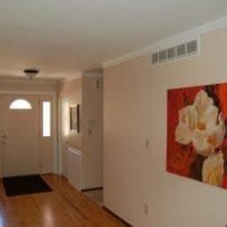 A hallway with wooden flooring leading to a front door, adorned with wall art.
