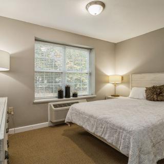 A cozy bedroom with a neatly made bed, soft lighting, and a window view.