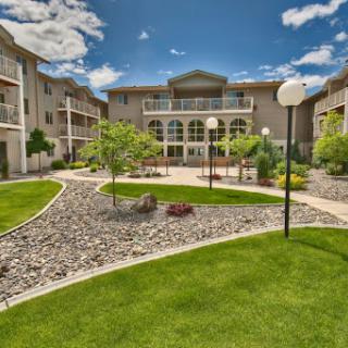 A beautifully landscaped apartment complex featuring green lawns, decorative pathways, and a bright blue sky.