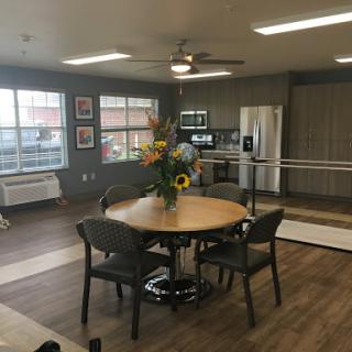 A contemporary dining area featuring a round table with seating, complemented by a floral centerpiece and modern kitchen appliances.