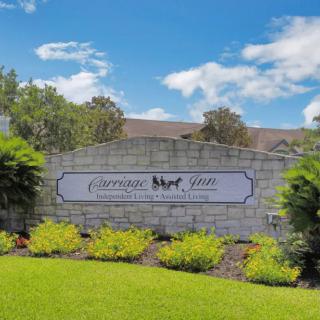A welcoming neighborhood entrance sign set against a stone wall with well-maintained landscaping and a clear blue sky.