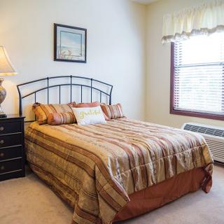 A cozy bedroom with a neatly made bed, a bedside lamp, and a window letting in natural light.