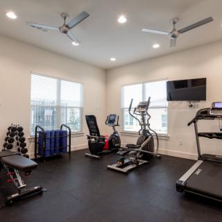 A modern gym room with various exercise equipment including a treadmill, elliptical machine, stationary bike, and weights.