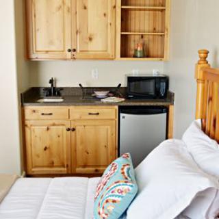 A small kitchenette setup next to a bed with wooden cabinets, microwave, and refrigerator.