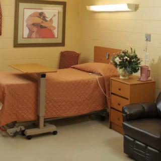 A well-furnished hospital room with a bed, bedside table, and a comfortable chair.