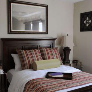 A cozy bedroom with a neatly made bed featuring striped pillows, a decorative mirror above the headboard, and elegant bedside lamps.