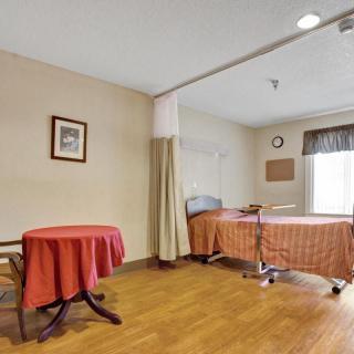 A shared hospital room with two beds separated by a curtain, featuring a small round table and a window providing natural light.