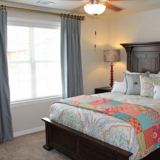 A cozy bedroom with a colorful bedspread, dark wood furniture, and large window with gray curtains.