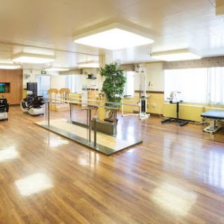 A spacious and well-lit rehabilitation center designed for physical therapy sessions, featuring wooden flooring and modern equipment.