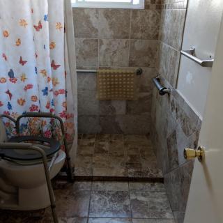 A bathroom with a shower area, tiled walls, and a portable toilet next to a colorful curtain.