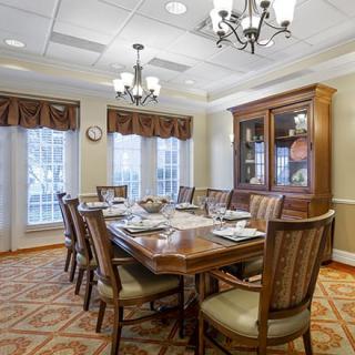 An elegant dining room with a large wooden table, surrounded by chairs and illuminated by a chandelier.
